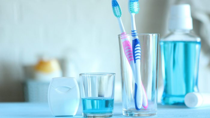 Cup with toothbrushes inside next to mouthwash and floss