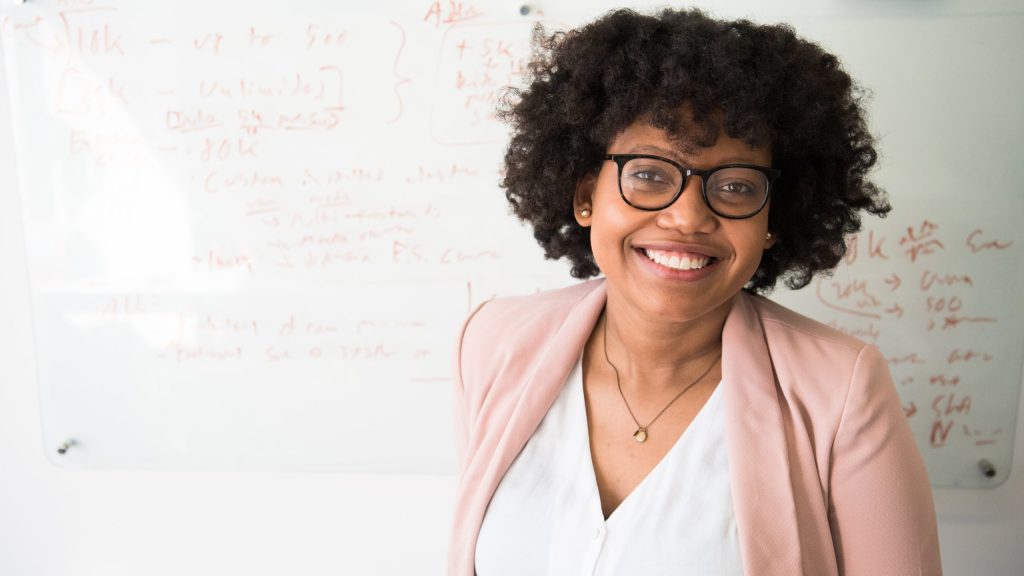 Woman Wearing Glasses Smiling In Front Of A Whiteboard