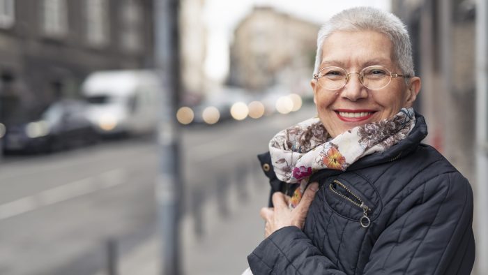 Portrait Of Beautiful Senior Woman With A Jacket On A Windy Day In An Urban City Environment, Happy And Cheerful