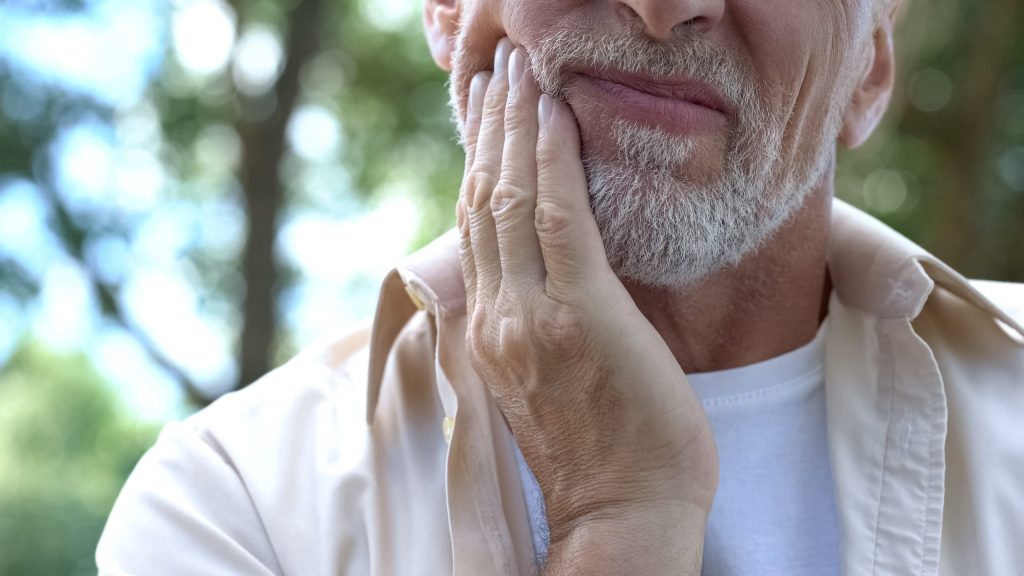Older man with white beard holding side of face in pain